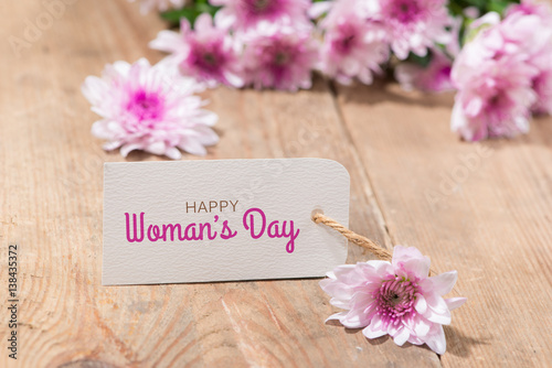 Womans Day tag paper with color flowers on wooden background. Top view.