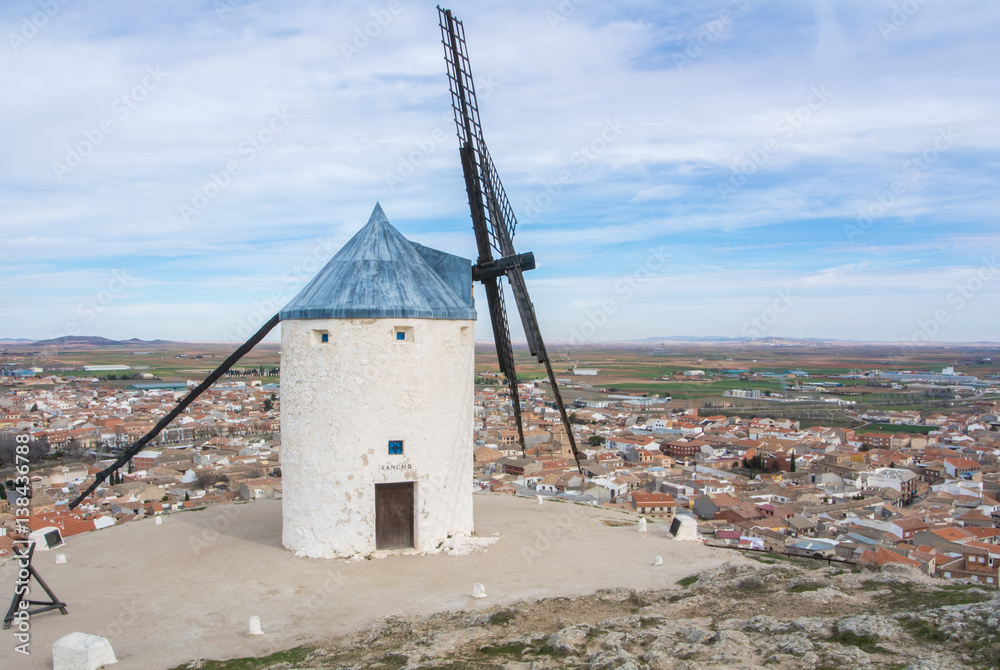 White old windmill on the hill near Consuegra (Castilla La Mancha, Spain), a symbol of region and journeys of Don Quixote (Alonso Quijano) and a town on cloudy day.