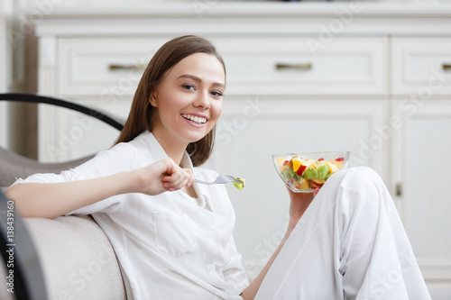 Young woman eating healthy fruit breakfast in bowl at home