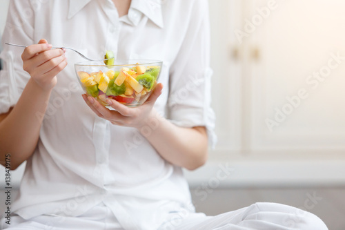 Young woman eating healthy fruit breakfast in bowl at home