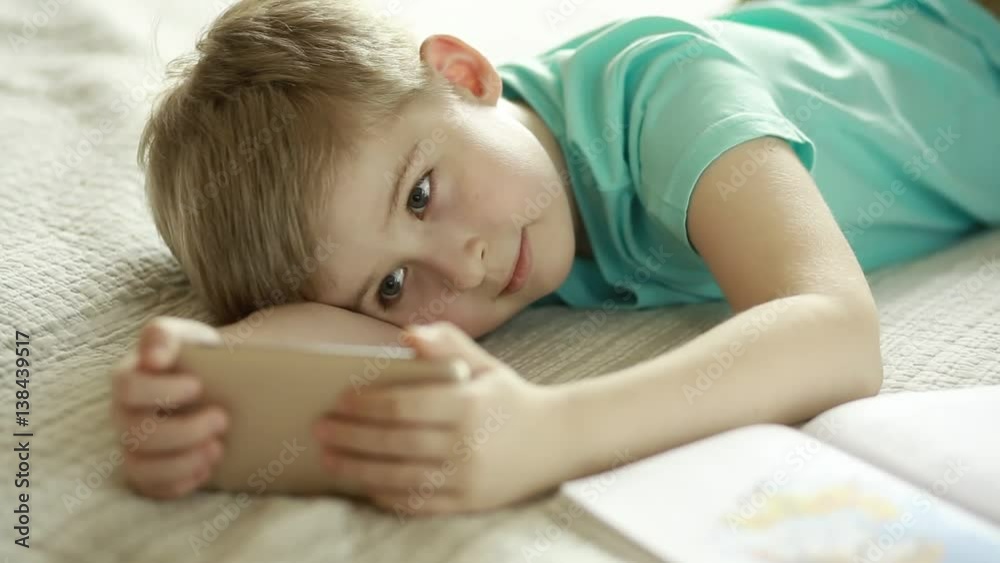 Funny boy looking in smart phone lying on a bed. Funny boy looking in smart phone lying on a bed.