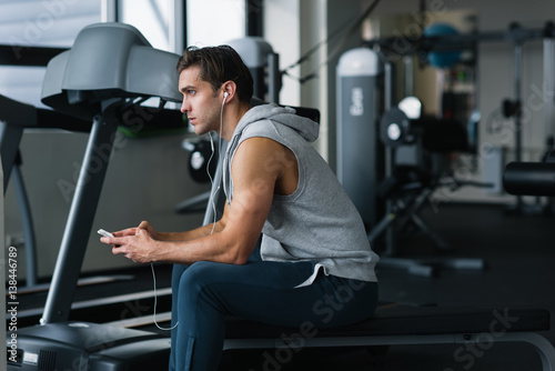 Young man using his phone while resting after working out in gym