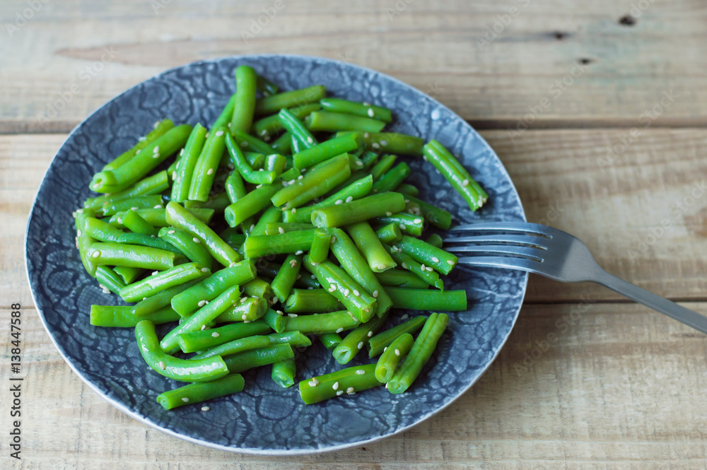Green beans mixed with sesame seeds served on a gray plate with fork on wooden table. Diet eating concept Green beans mixed with sesame seeds served on a gray plate with fork on wooden table. Diet eating concept