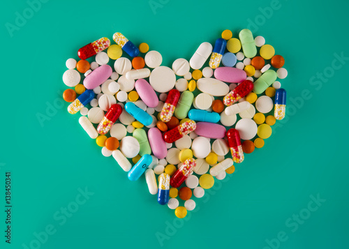 Multicolored pills and tablets, heart shape on green background