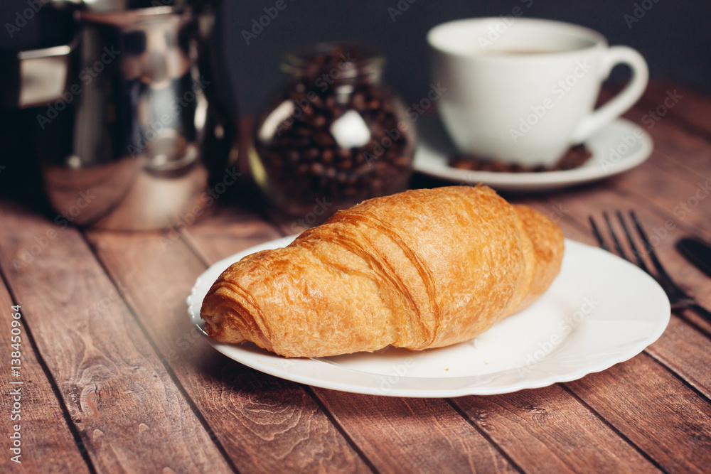 Croissant in a white plate, a jar with coffee beans, a cup in the background Croissant in a white plate, a jar with coffee beans, a cup in the background