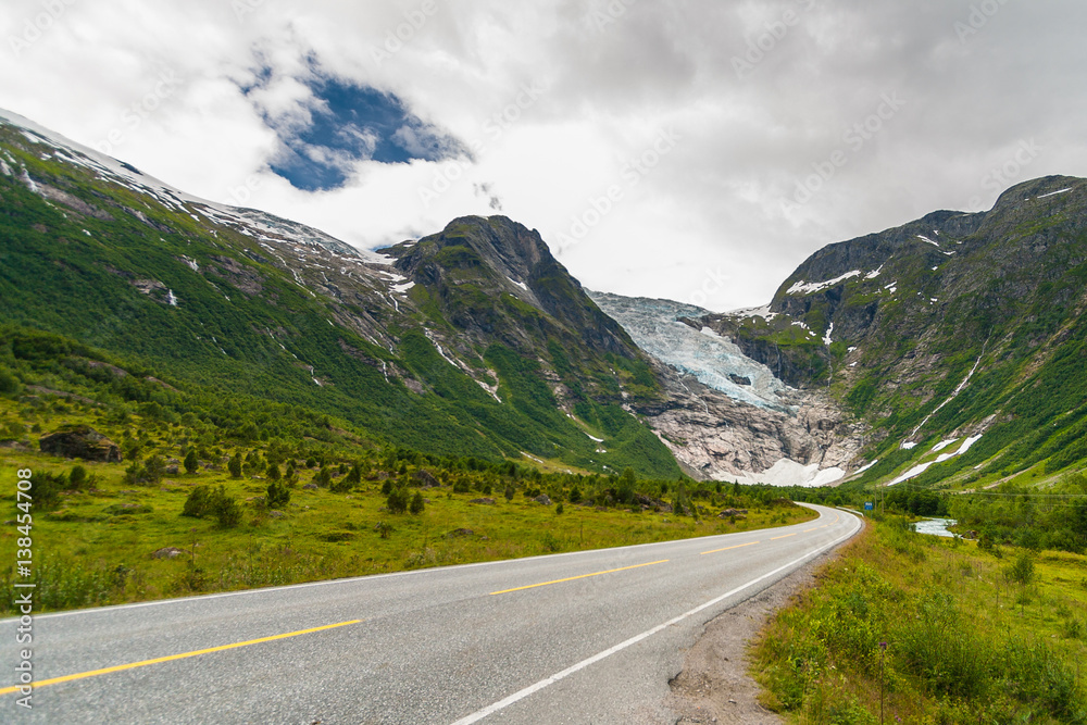 Naklejka premium Norwegian country road in the summer among the mountains. Boyabreen glacier in the background. Sogndal Municipality in Sogn og Fjordane county. Norway.