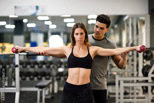 Personal trainer helping a young woman lift weights