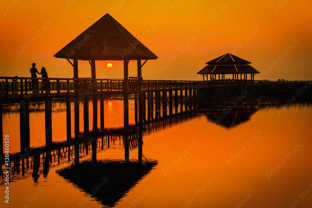 Silhouette old wooden bridge and pavilion in lake at sunset