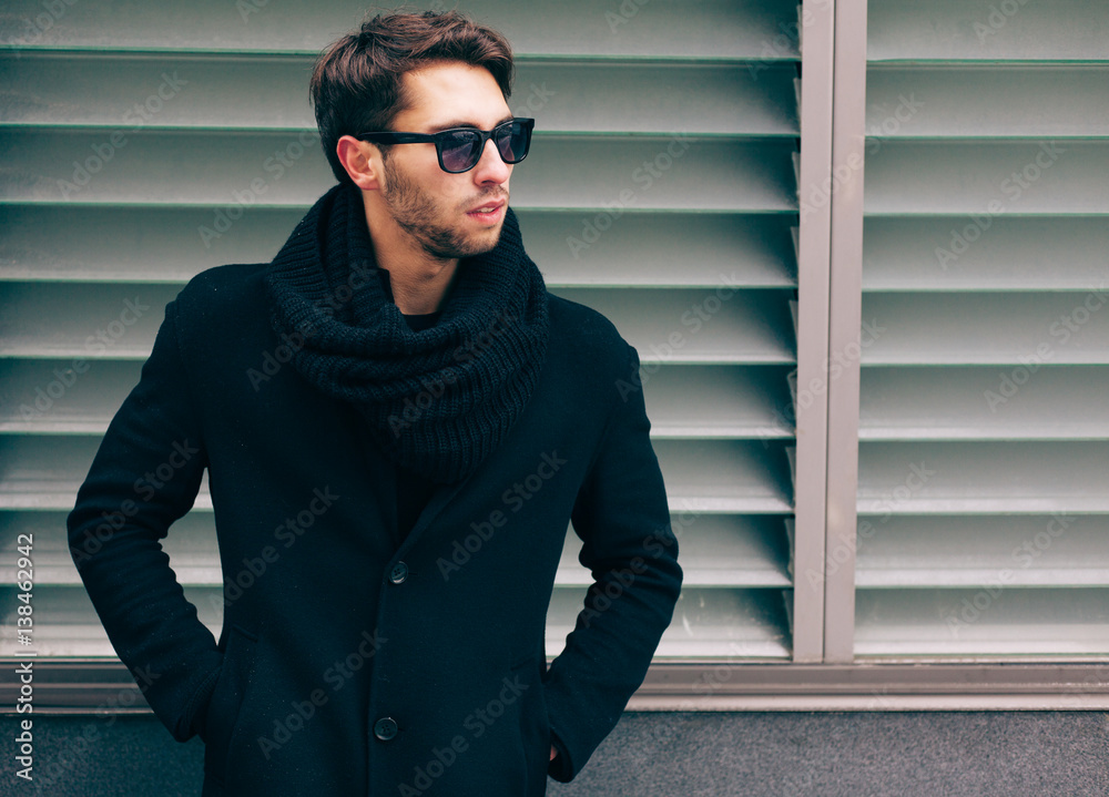 Portrait of young trendy man wearing a black coat with a snoot in sunglasses. Street style. Fashion.