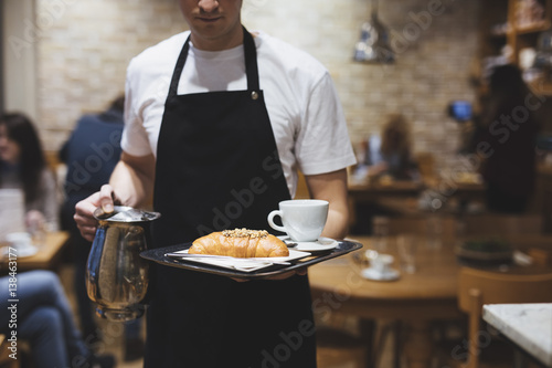 Unrecognisable waiter holding a tray with coffee and croissant.