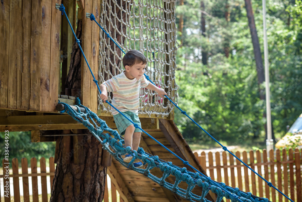 Little climber takes the rope bridge. Boy has fun time, kid climbing on sunny warm summer day Little climber takes the rope bridge. Boy has fun time, kid climbing on sunny warm summer day