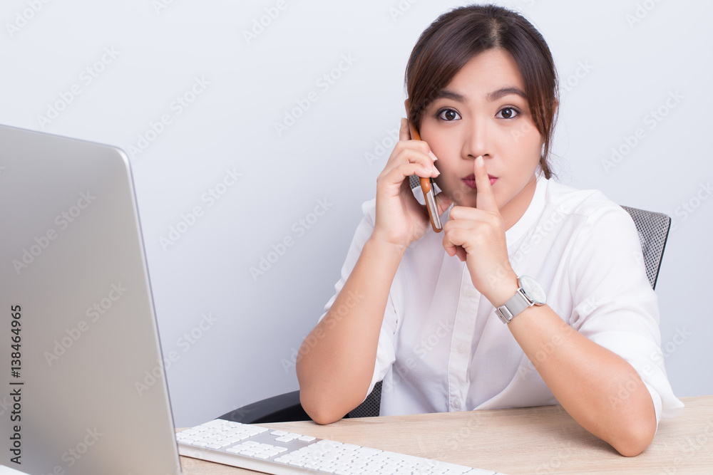 Woman calling the phone and make quiet gesture in office Woman calling the phone and make quiet gesture in office