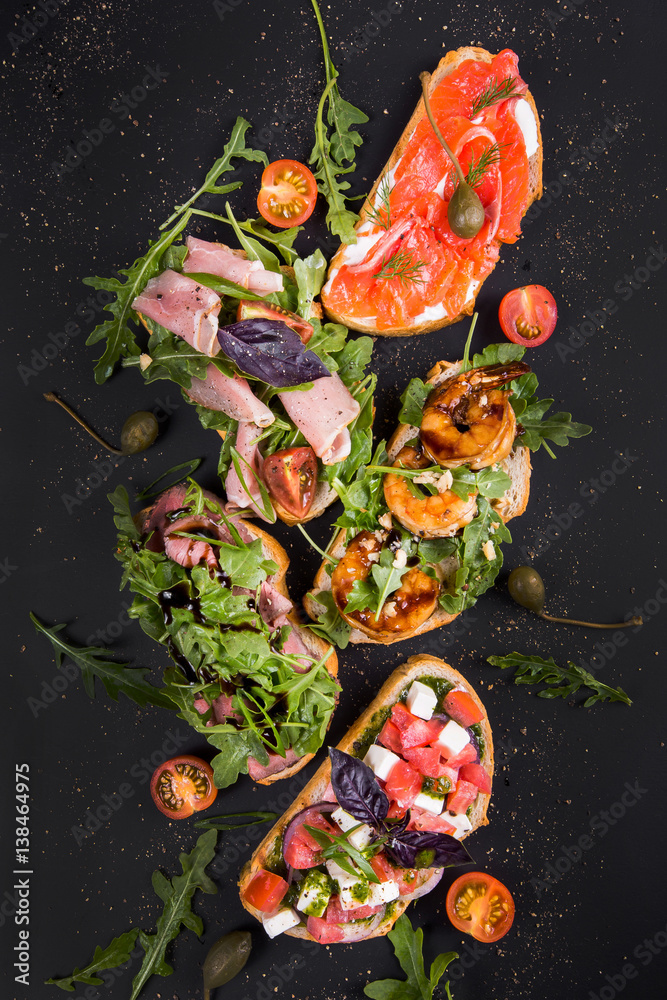 Brushetta set for wine. Variety of small sandwiches with prosciutto, tomatoes, parmesan cheese, fresh basil and balsamic creme on dark background. top view.