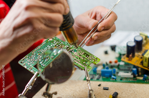 Engineer soldering microcircuit though magnifier. third hand