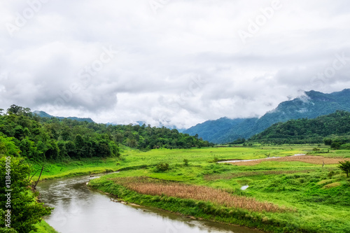 Green field and curved river in fog mountain