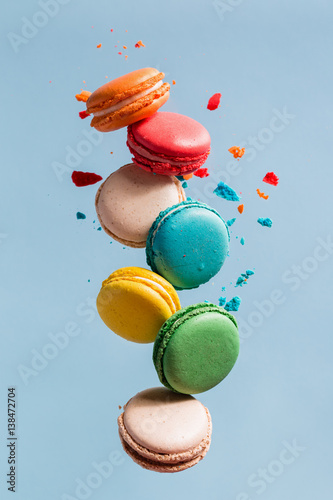 Different types of macaroons in motion falling on light blue background. 