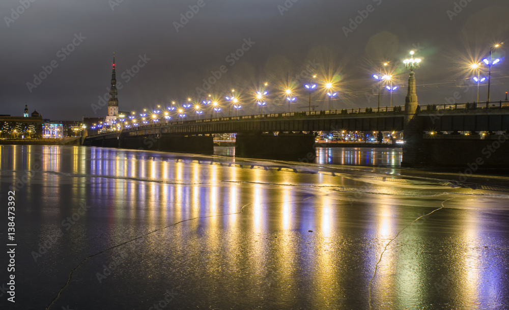 illuminated stone bridge Akmens tilts leading over the frozen river Daugava to the St. Peter's Church in the old part of the city of Riga, Latvia on a cold winter evening