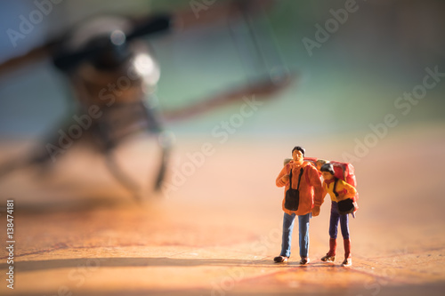 Miniature people : young couple standing in front of vintage airplane for travelling around the world, exploring on earth background concept.