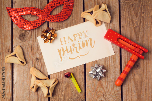 Jewish holiday Purim concept with greeting card with text and hamantaschen cookies on wooden background. Top view from above