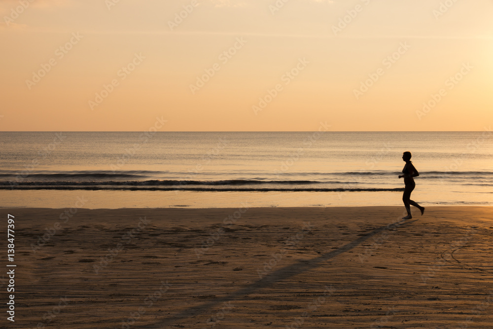 Woman running on the beach at sunset, healthy lifestyle