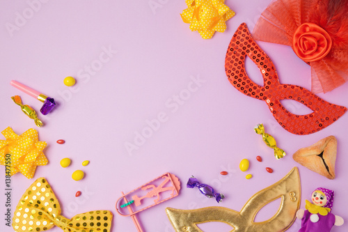 Purim holiday concept with carnival mask and party supplies on purple background. Top view from above. Flat lay
