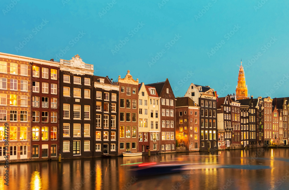 Houses facades over canal with reflections illuminated at night, Amsterdam.