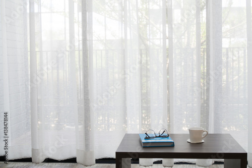 office desk with modern glasses on book, white coffee cup on white drape background texture at living room.