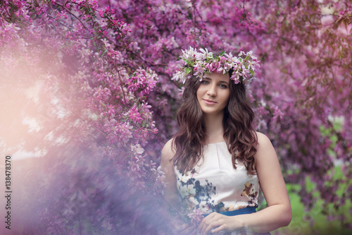 happy young woman with a wreath on his head in the blossoming spring garden