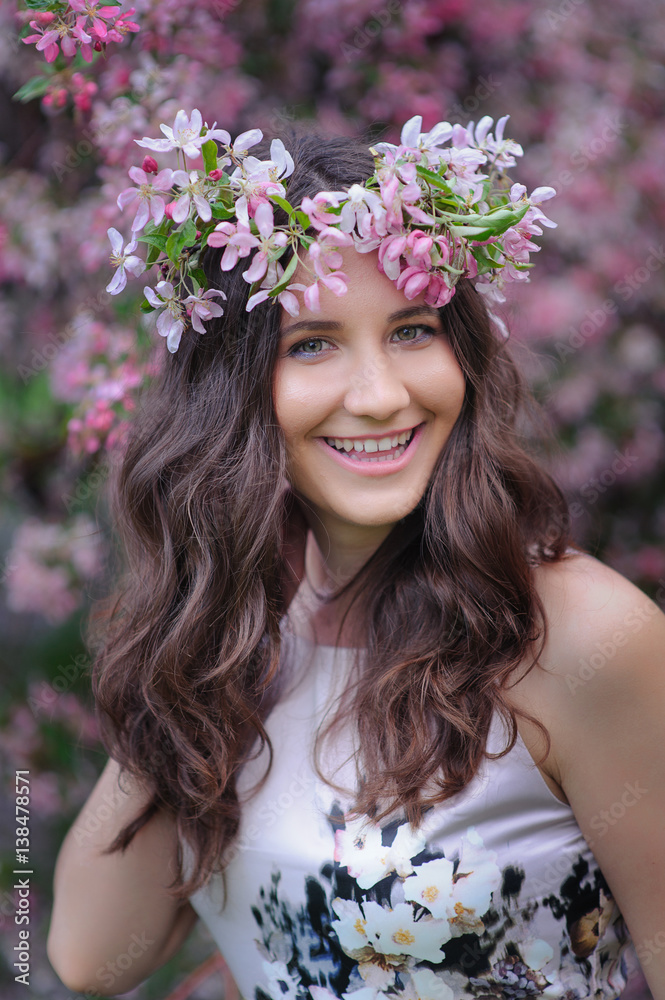 Fototapeta premium smiling young woman with a wreath on her head on a background of flowering spring trees