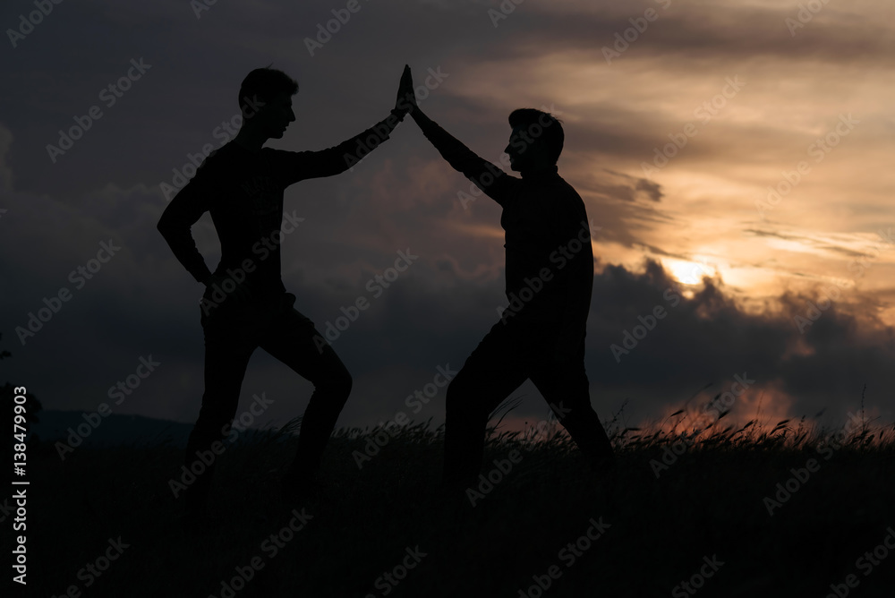 teamwork of two man at the top of mountain. silhouette at sunset
