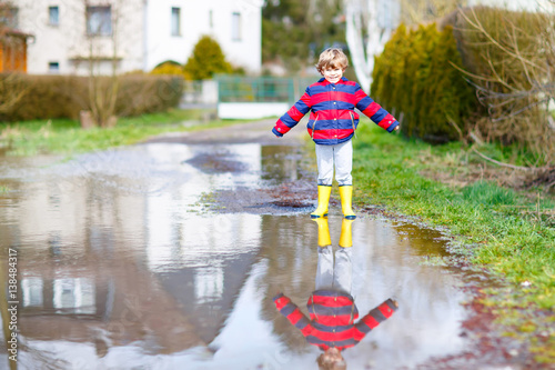 Little kid boy jumping through rain puddle