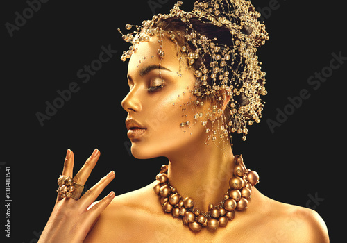 Gold woman skin. Beauty fashion model girl with golden makeup, hair and jewellery on black background © Subbotina Anna