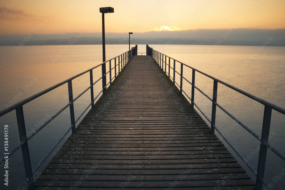 Ein symmetrischer ruhiger Holzsteg am Bodensee bei Sonnenuntergang 