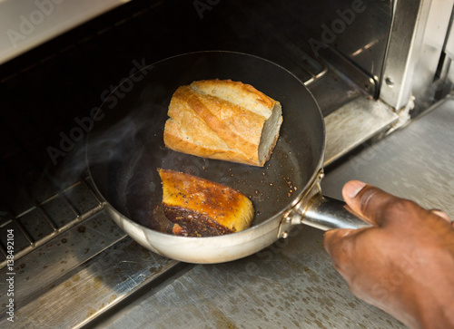 Foie gras and a crusty bread roll being  cooked in an oven.