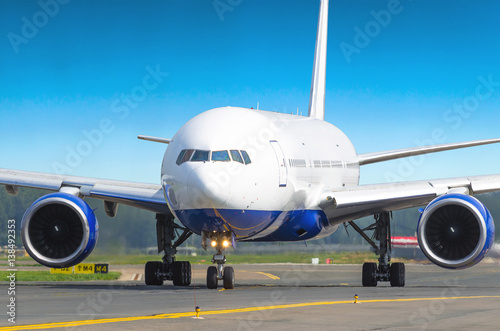 Big aircraft in airport taxis on the runway on a background of blue sky