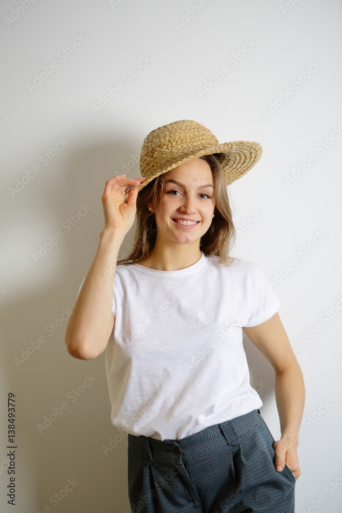 Young beautiful smiling woman holding a straw hat hand, the other hand in his pocket Young beautiful smiling woman holding a straw hat hand, the other hand in his pocket
