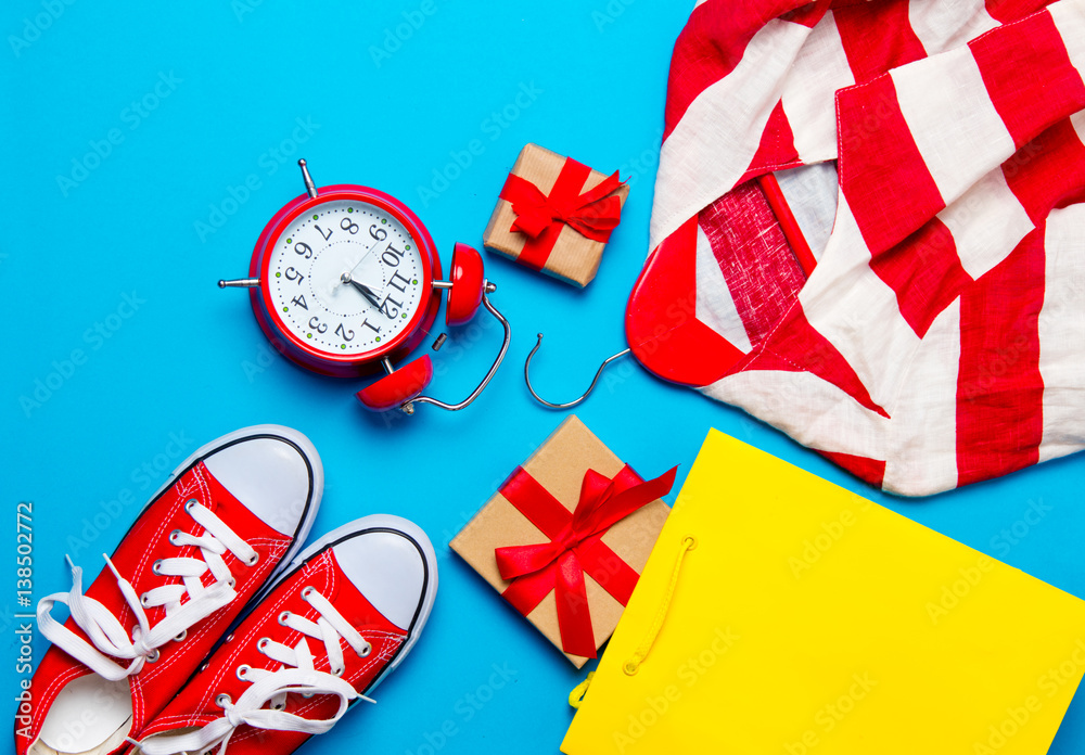 Fototapeta premium big red gumshoes, cool shopping bag, striped jacket on hanger, alarm clock and beautiful gifts on the wonderful blue background
