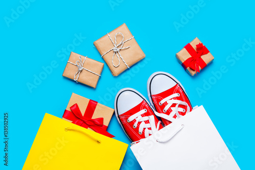 big red gumshoes in cool shopping bag and beautiful gifts near other shopping bag on the wonderful blue background photo