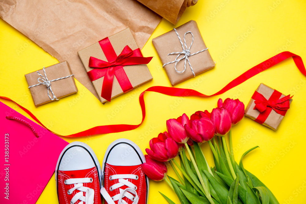 Fototapeta premium bunch of red tulips, red gumshoes, cool shopping bag, things for wrapping and beautiful gifts on the wonderful yellow background