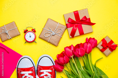 bunch of red tulips, red gumshoes, cool shopping bag, alarm clock and beautiful gifts on the wonderful yellow background