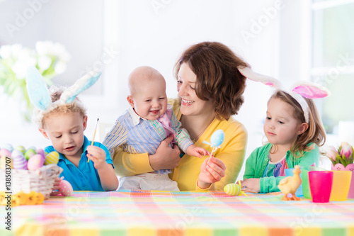 Mother with three children painting Easter eggs