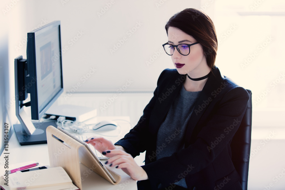 © Masson - beautiful young woman sitting at the desk and typing text on tablet in the cool bright office