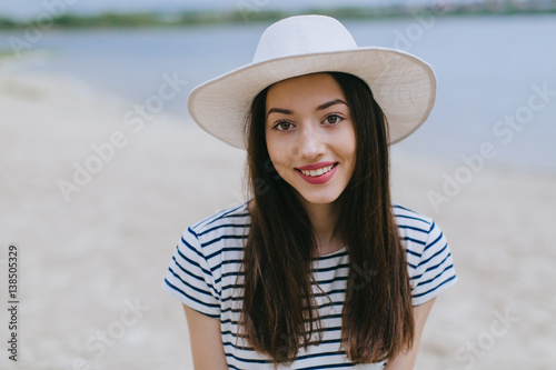 Stylish and fashionable girl in white hat posing on the summer beach.