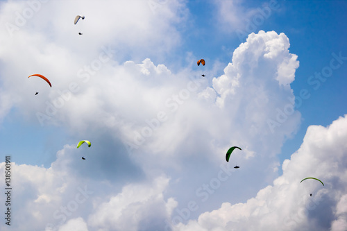 Bild auf Leinwand Paragliders fly among the white clouds on a sunny day