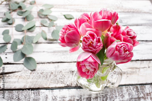 pink piony type tulips in tall glass jar on edge of white wooden rustic table. Spring melody mood of love