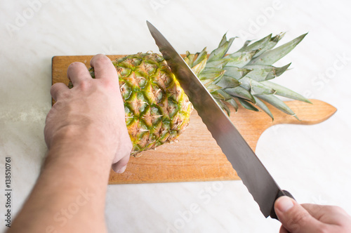 Hands cutting  pineapple on a wooden board