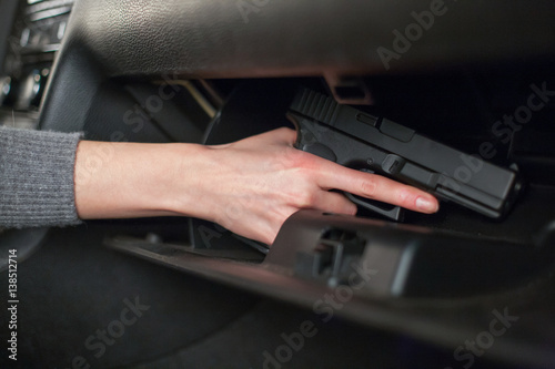 The female hand pulls out a gun from the glove box in the car.