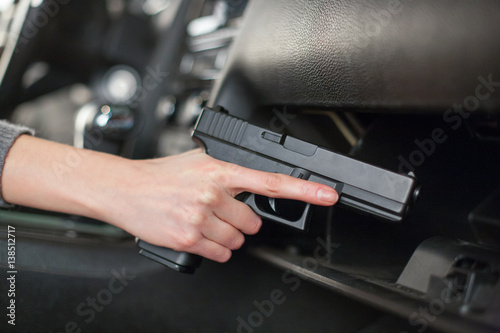 The female hand pulls out a gun from the glove box in the car.