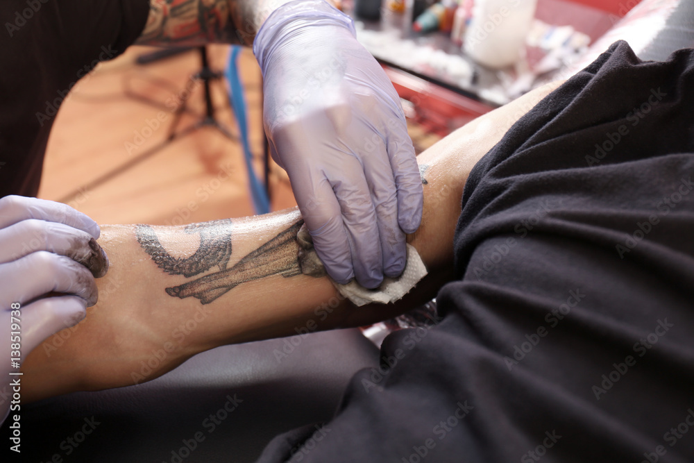 Hand of professional artist wiping finished tattoo with hygienic napkin, close up view