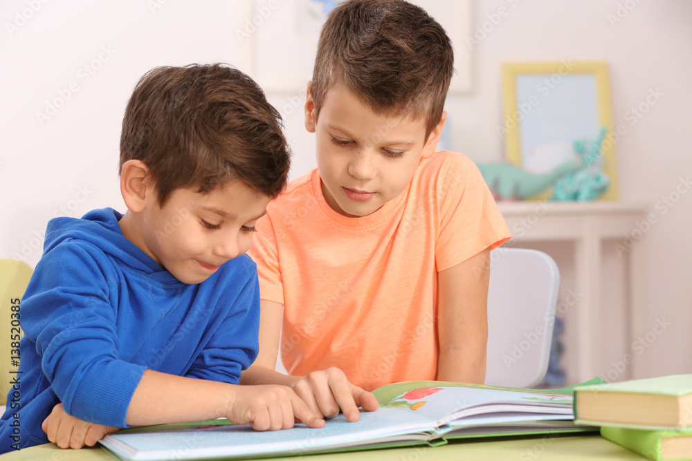 Cute little boys with book sitting at table, closeup Cute little boys with book sitting at table, closeup